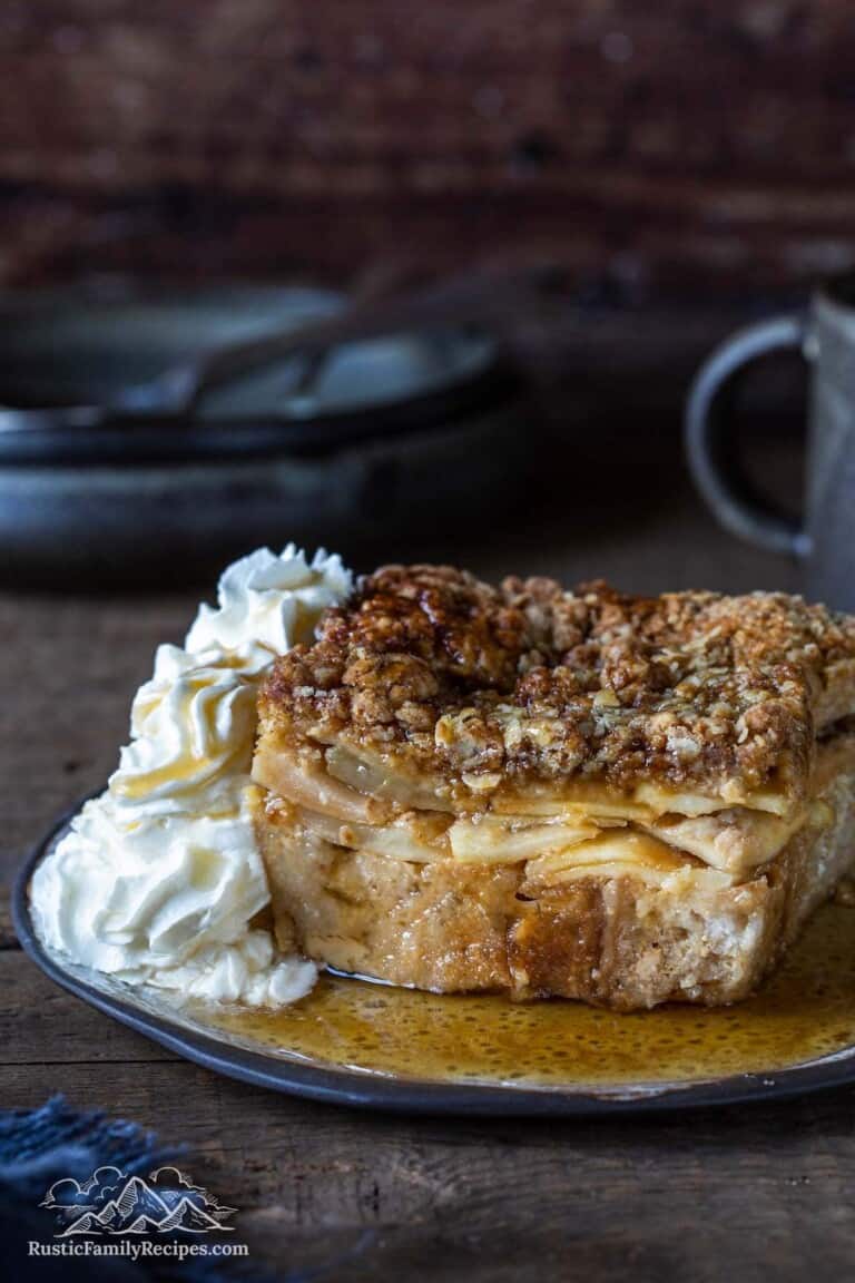 A slice of baked french toast apple casserole on a plate with whipped cream