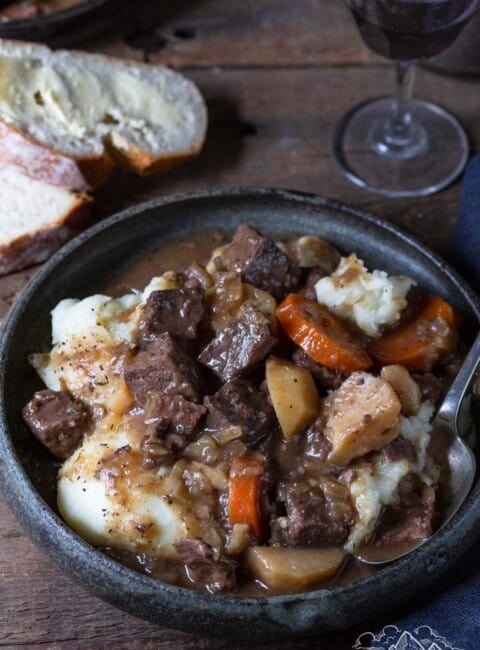 A bowl filled with deer meat stew next to buttered slices of bread