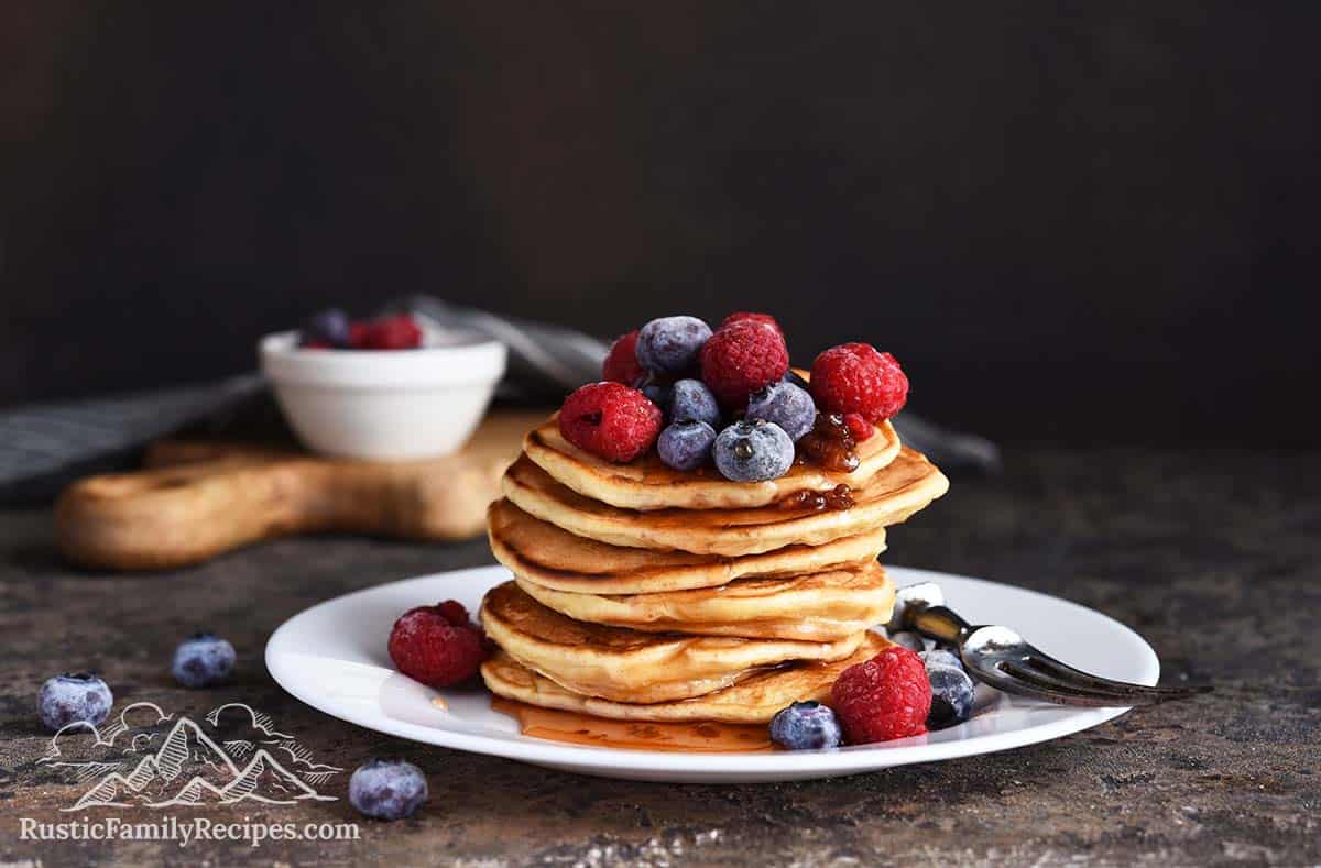 A tall stack of pancakes topped with berries and syrup