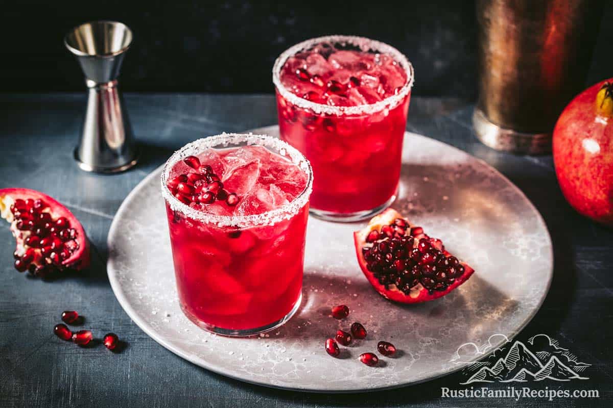 Two pomegranate margaritas next to sliced open pomegranate pieces