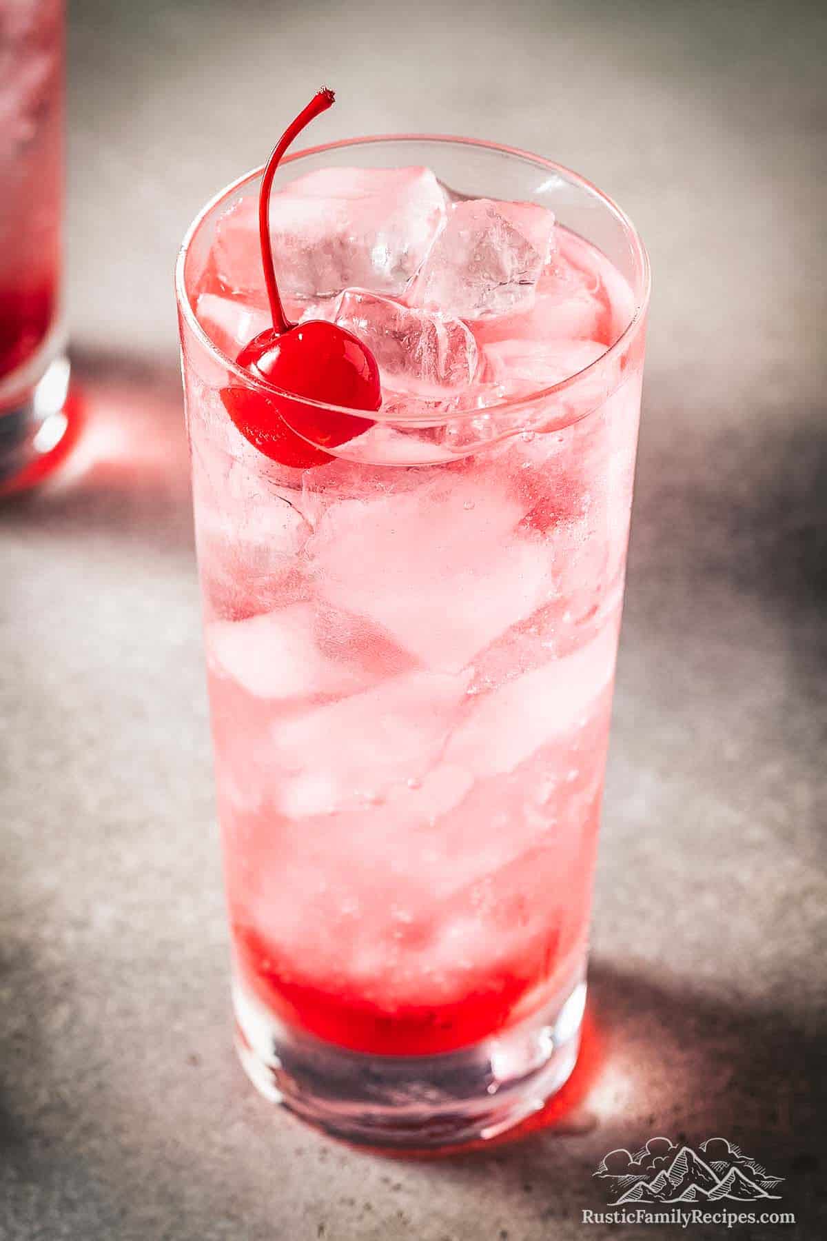 This Shirley Temple drink is a classic non-alcoholic cocktail. Made with ginger ale, grenadine, lime juice & a maraschino cherry. Shirley Temple drink in a tall glass with a cherry