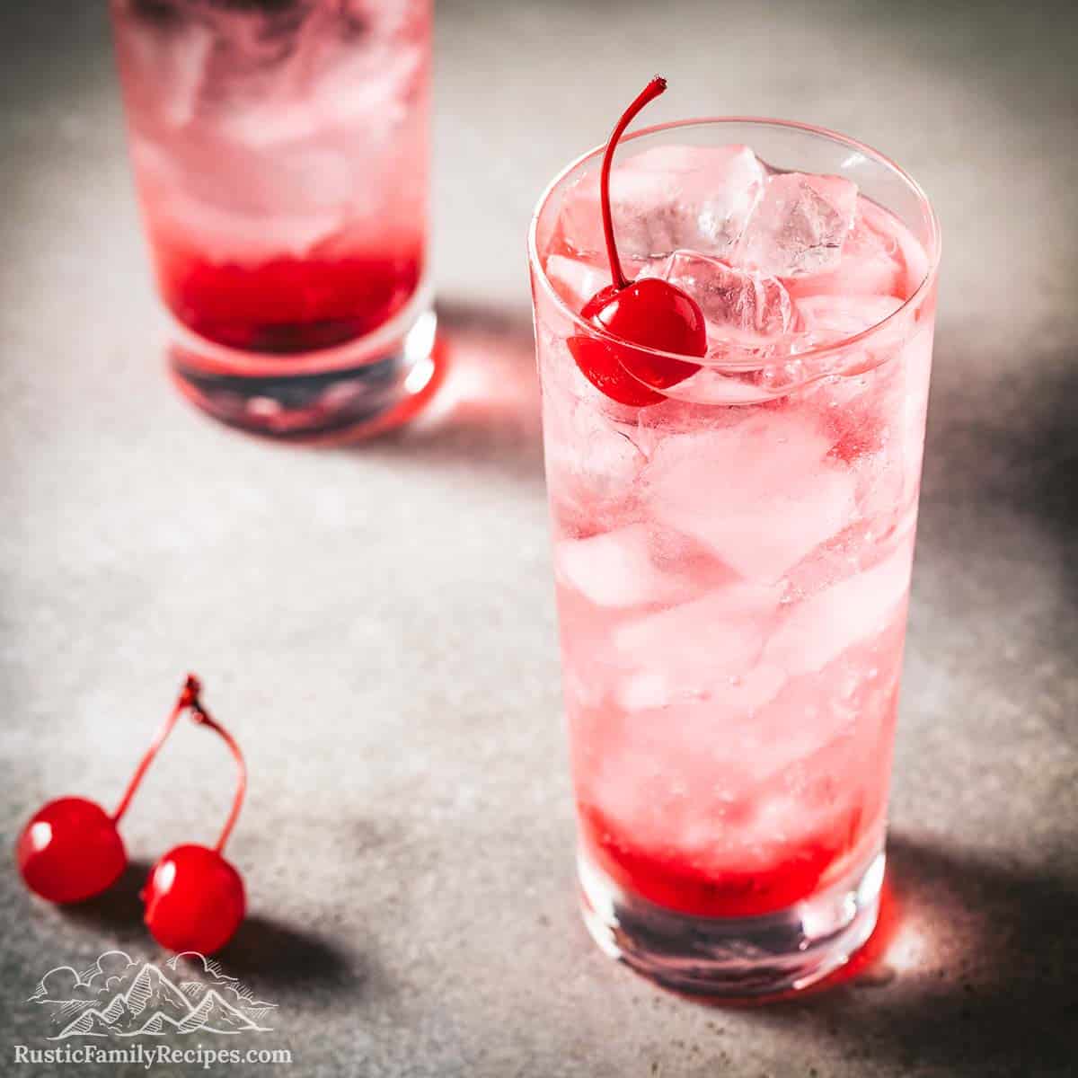 Two shirley temple drinks in tall glasses with cherries
