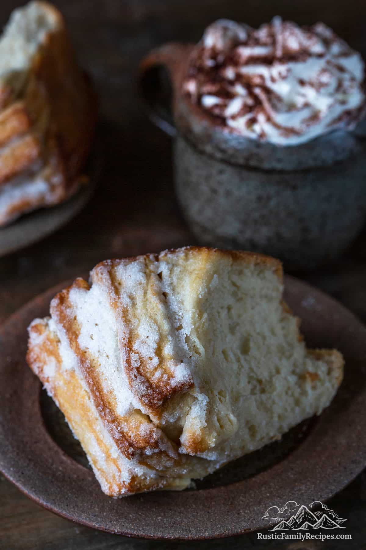 A slice of sugared monkey bread on a plate with a mug of hot cocoa.