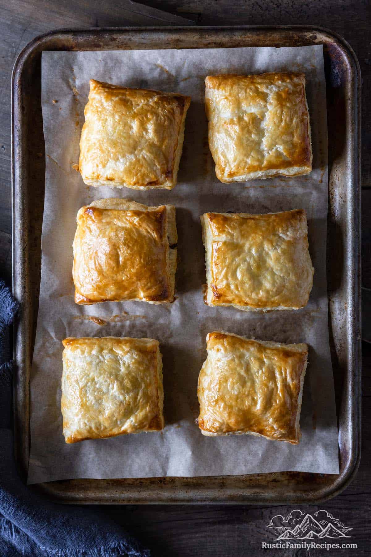 Rows of baked venison meat pies on a parchment lined baking sheet.