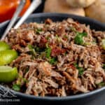 A bowl with pork carnitas and wedges of lime