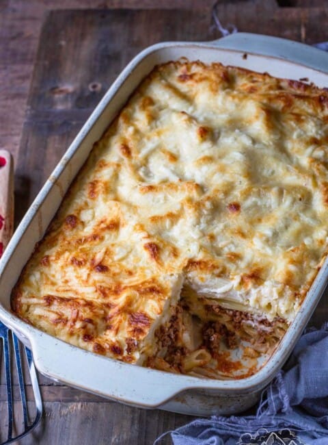 Golden baked Greek pastitsio pasta in a baking dish with a slice missing.