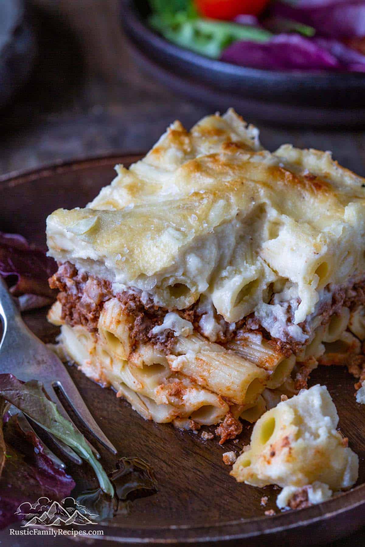 A slice of pastitsio with all its pasta, meat, and béchamel layers, on a plate with a fork.