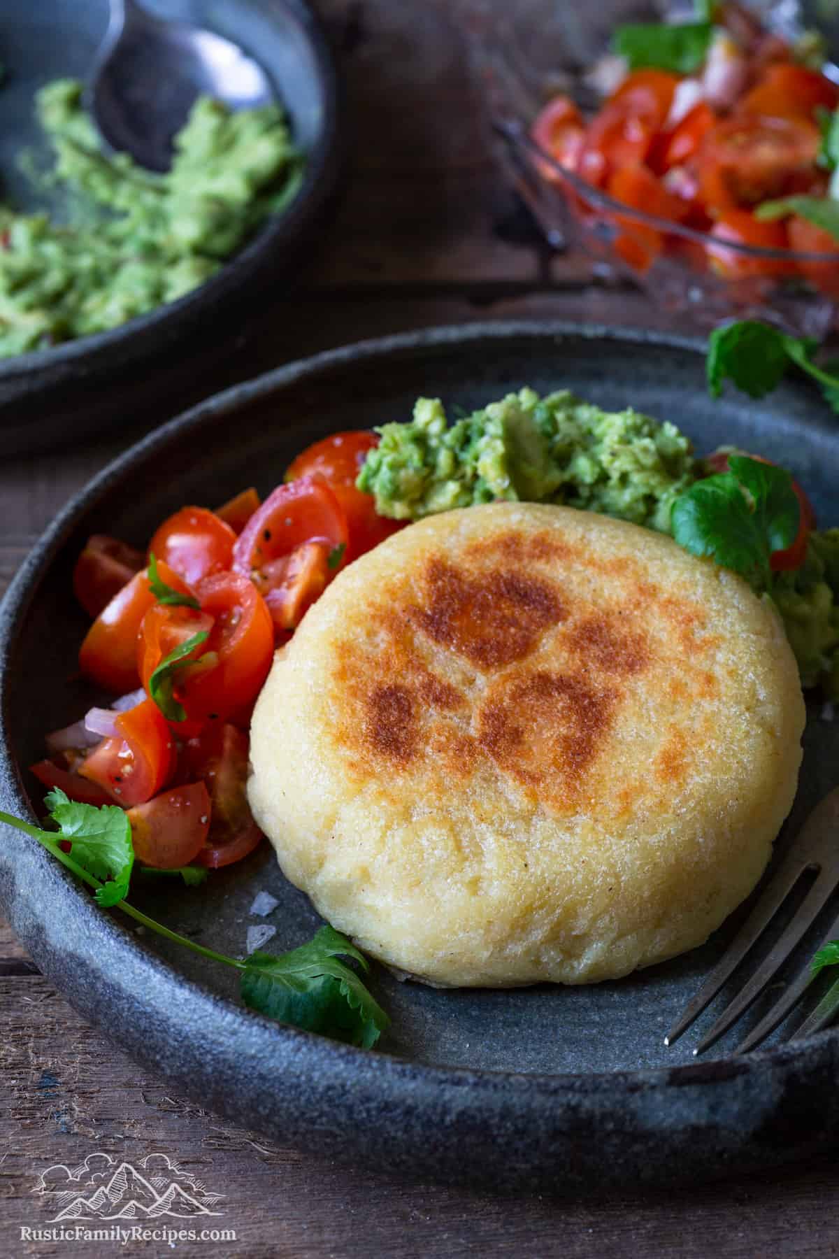 An arepa on a plate with salsa and guacamole