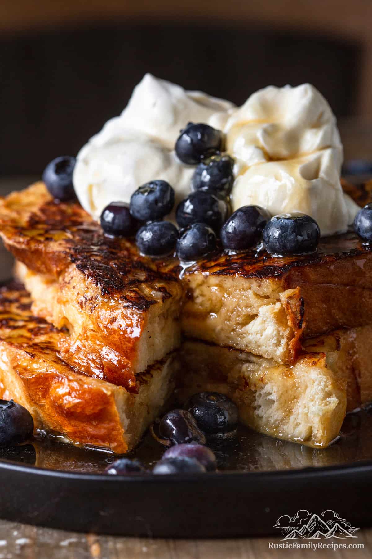 Two slices of challah french toast with a slice taken out, whipped cream and blueberries on top