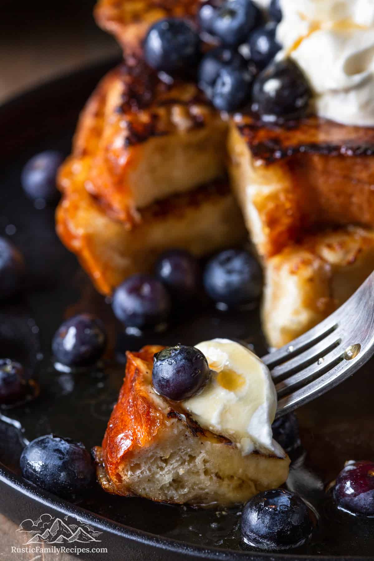 A fork with a bitefull of french toast, whipped cream and blueberries