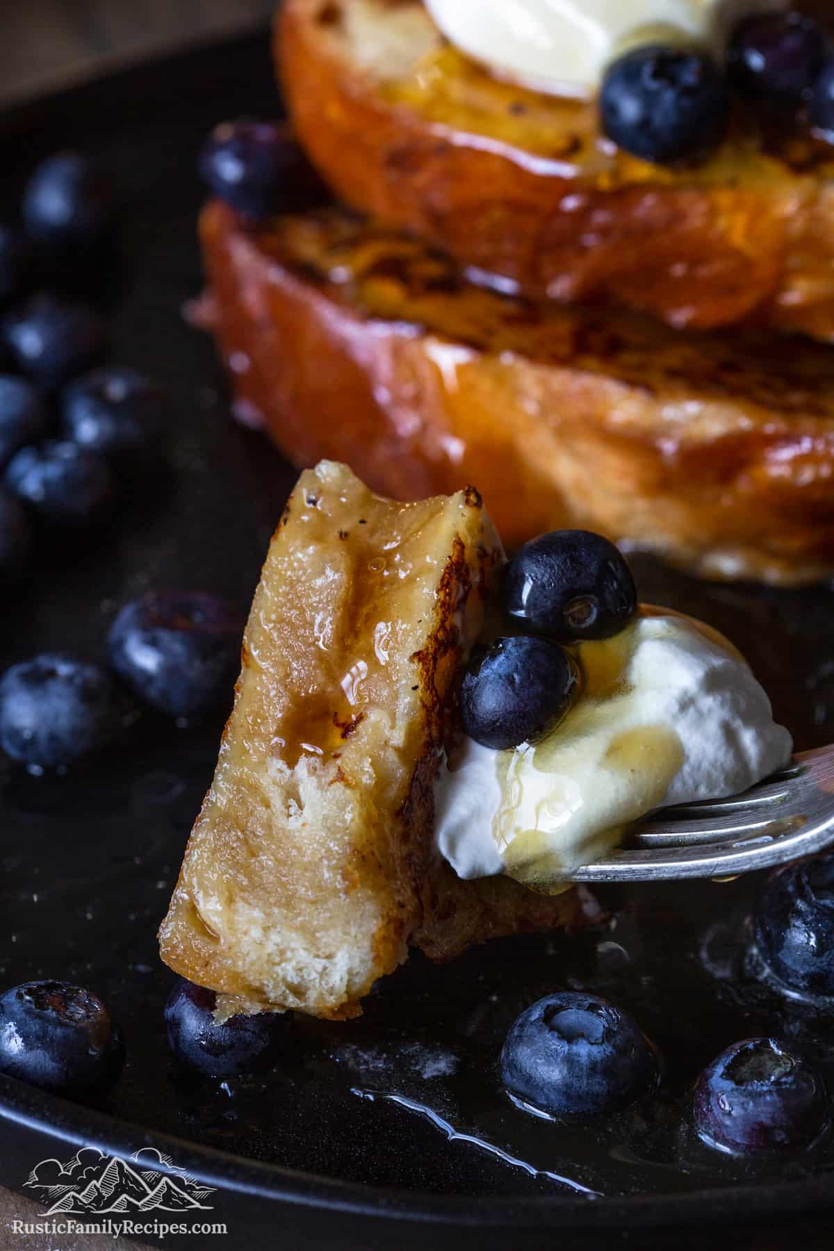 A fork with a bite full of french toast, whipped cream and blueberries