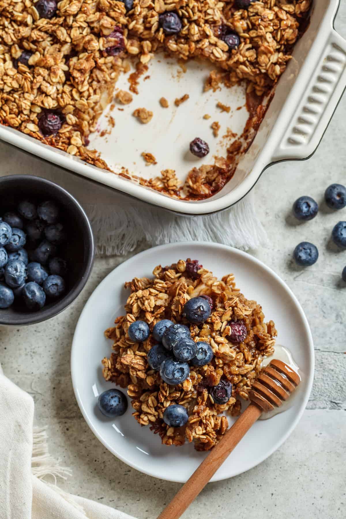 Blueberry Baked Oatmeal in a baking dish and on a plate with honey