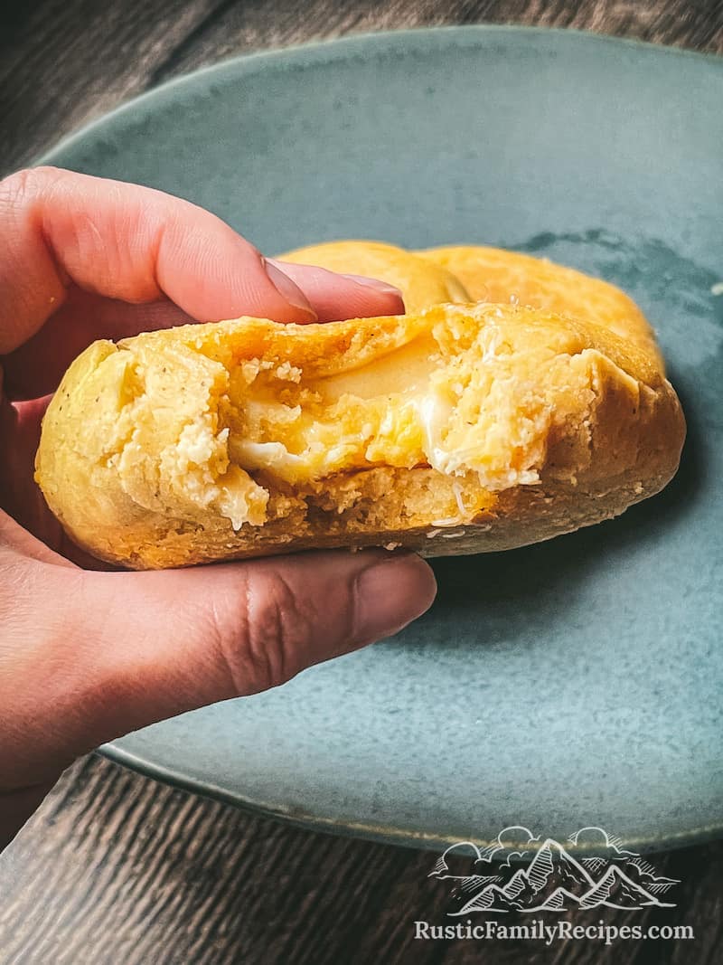 Hand holding an arepa filled with eggs and cheese, a bite taken out