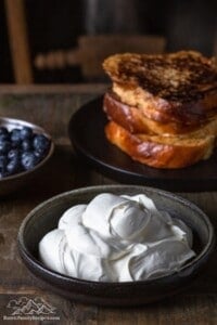A bowl with maple whipped cream in front of french toast and a bowl of blueberries