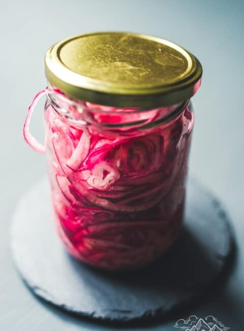 A mason jar with a lid filled with pickled red onions