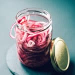 A mason jar filled with pickled red onions next to a metal lid
