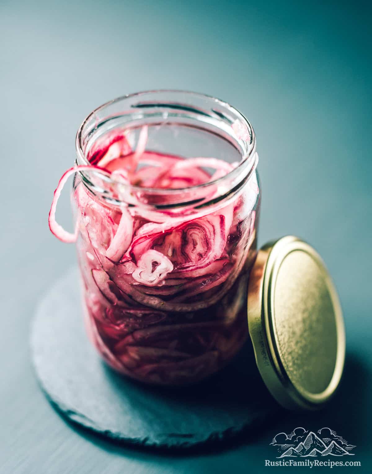 A mason jar filled with pickled red onions next to a metal lid