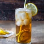 A tall glass filled with arnold palmer drink a lemon, and a straw
