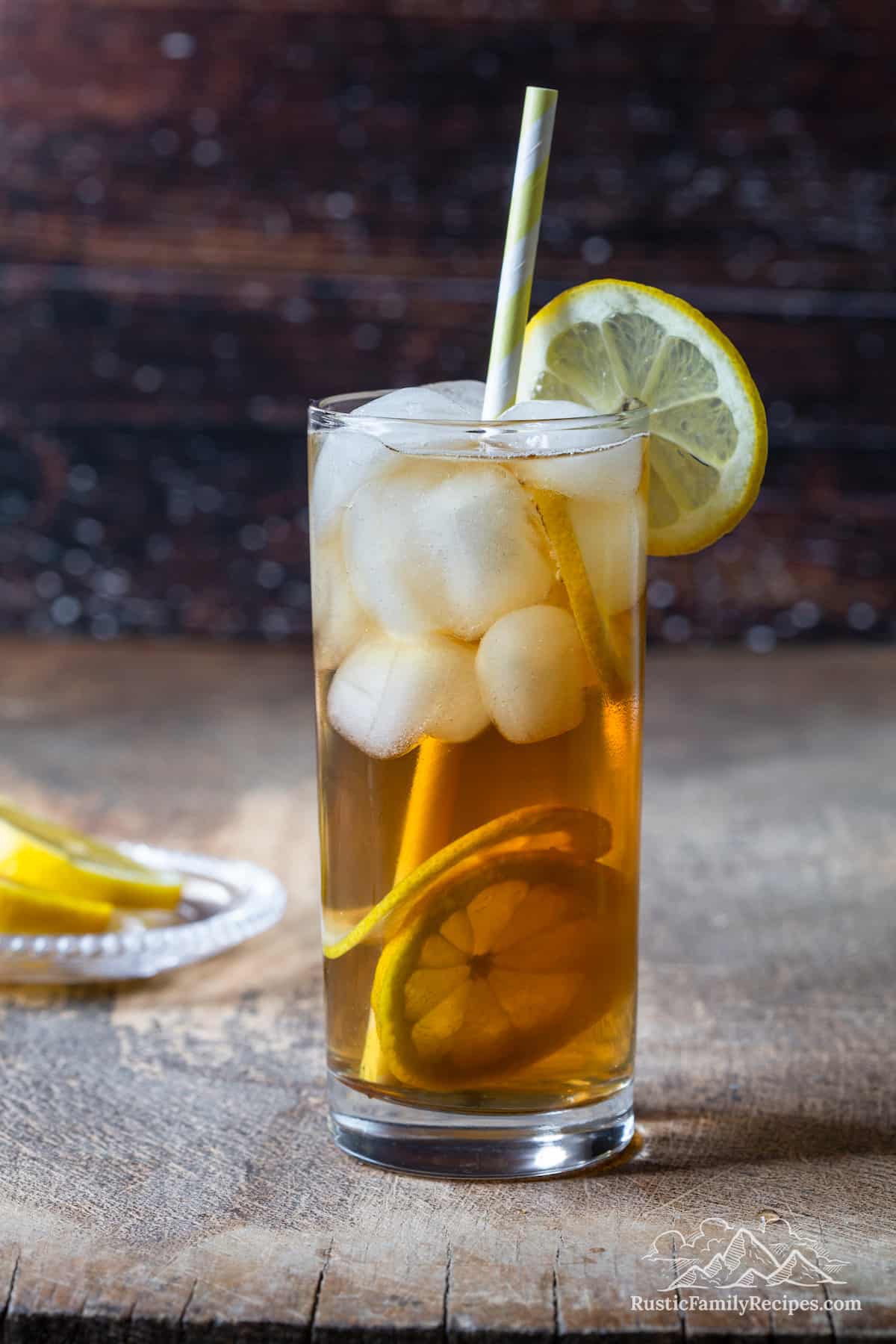 A tall glass filled with arnold palmer drink a lemon, and a straw