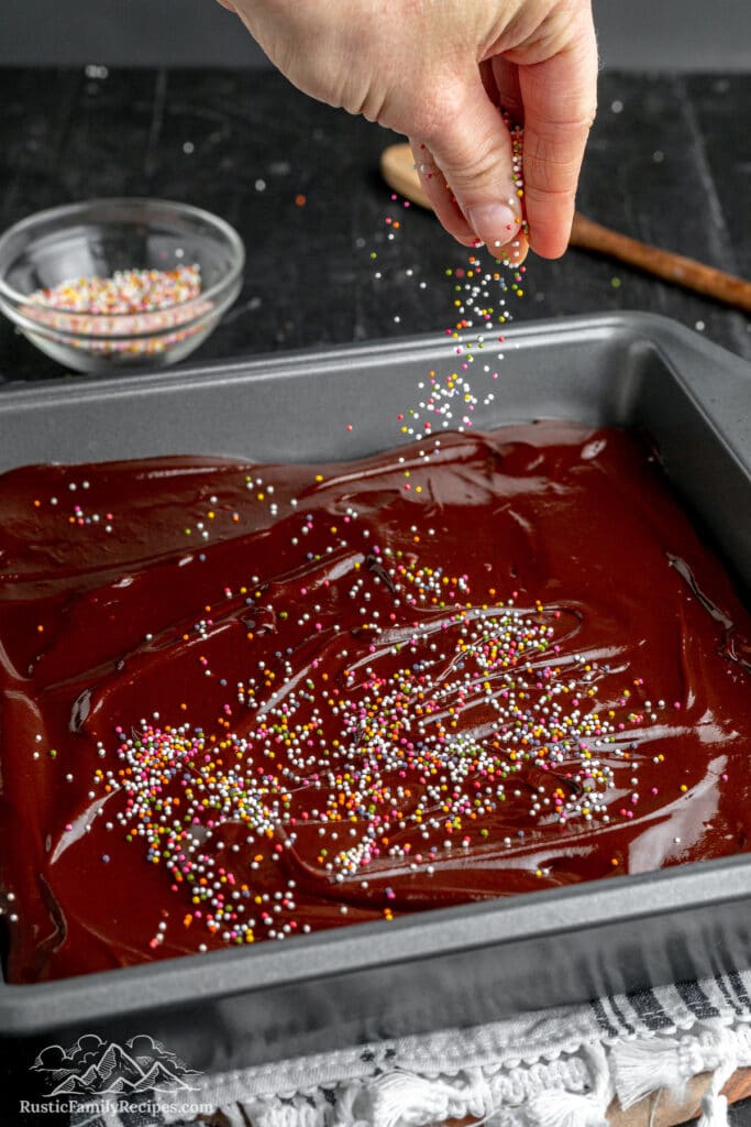Sprinkles being added on top of frosted brownies in a pan