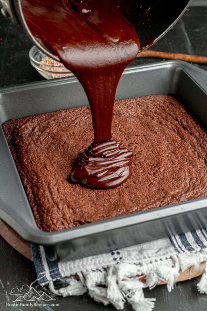 Chocolate frosting being poured over a pan of cooled brownies