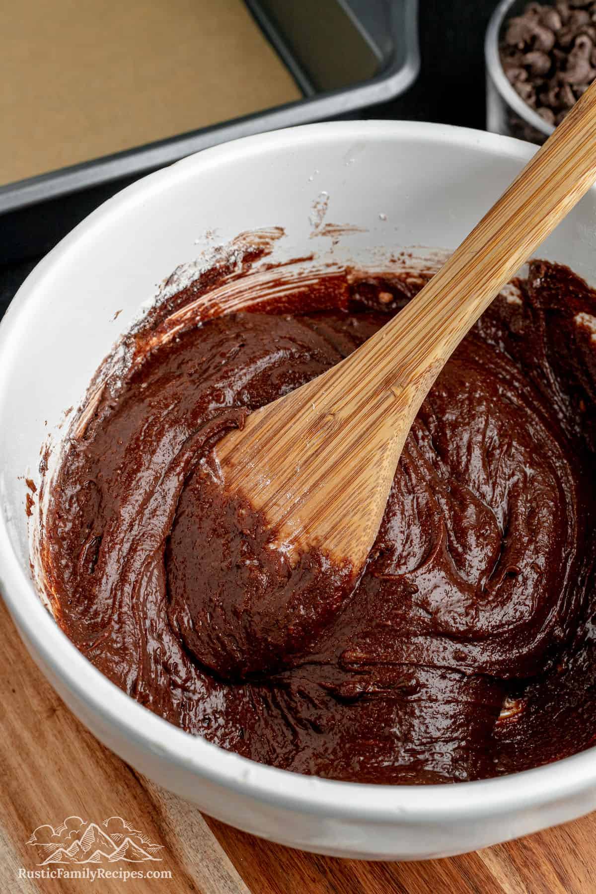A wooden spoon stirring brownie batter in a white bowl