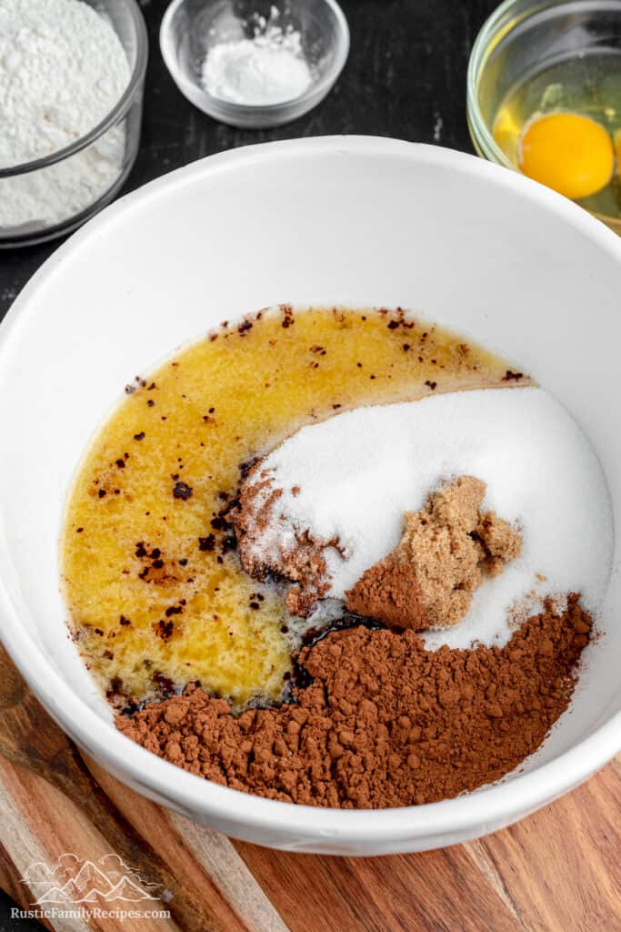 Melted butter, granulated sugar, cocoa powder and brown sugar inside of a mixing bowl