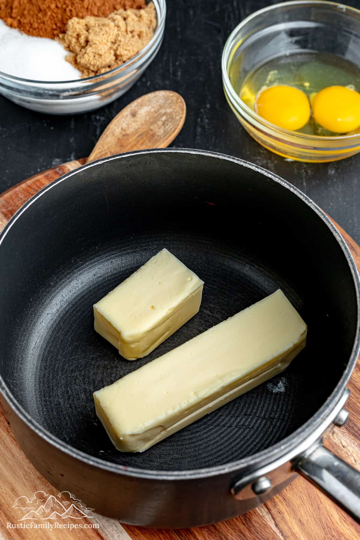 Butter inside of a metal skillet with a bowl of eggs in the background