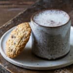A mug with moon milk and a cookie on a plate
