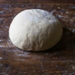 A ball of homemade pizza dough on a wood cutting board