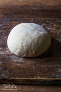 A ball of homemade pizza dough on a wood cutting board