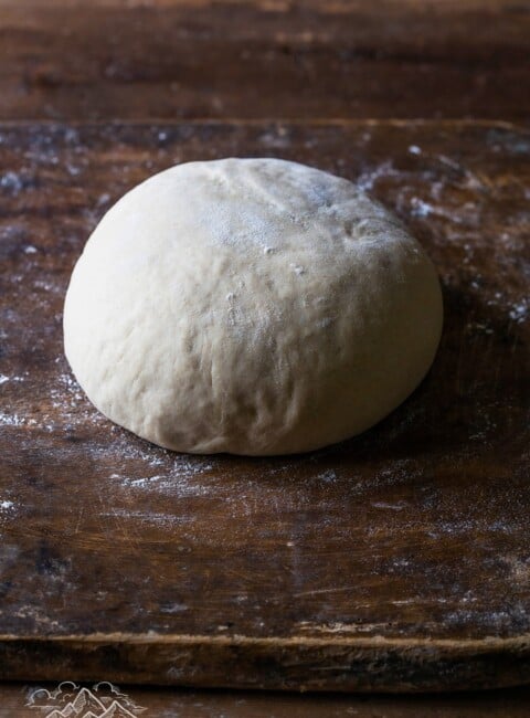 A ball of homemade pizza dough on a wood cutting board