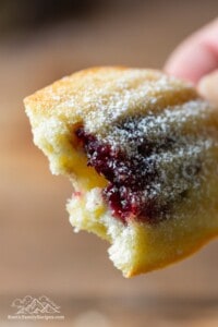Close up of a lemon tea cake with blueberry jam inside, a bite taken out.