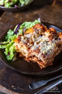 A slice of homemade lasagna on a plate with salad