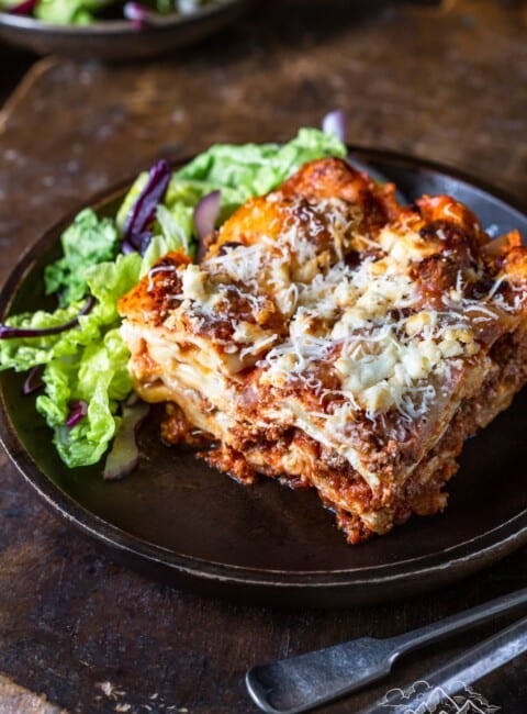 A slice of homemade lasagna on a plate with salad