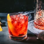 Negroni cocktail on the rocks with an orange peel and a mixing glass filled with ice