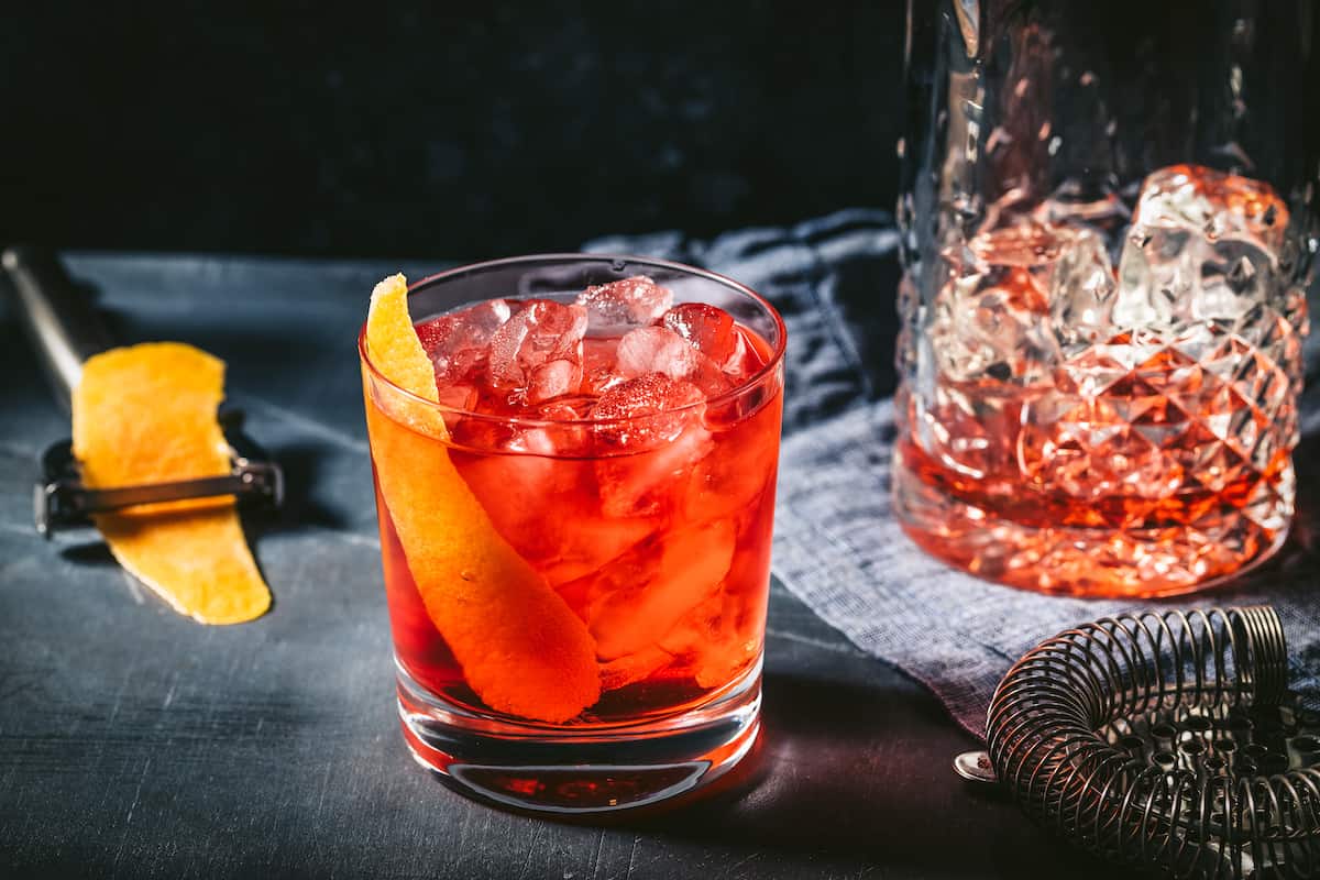 Negroni cocktail on the rocks with an orange peel and a mixing glass filled with ice