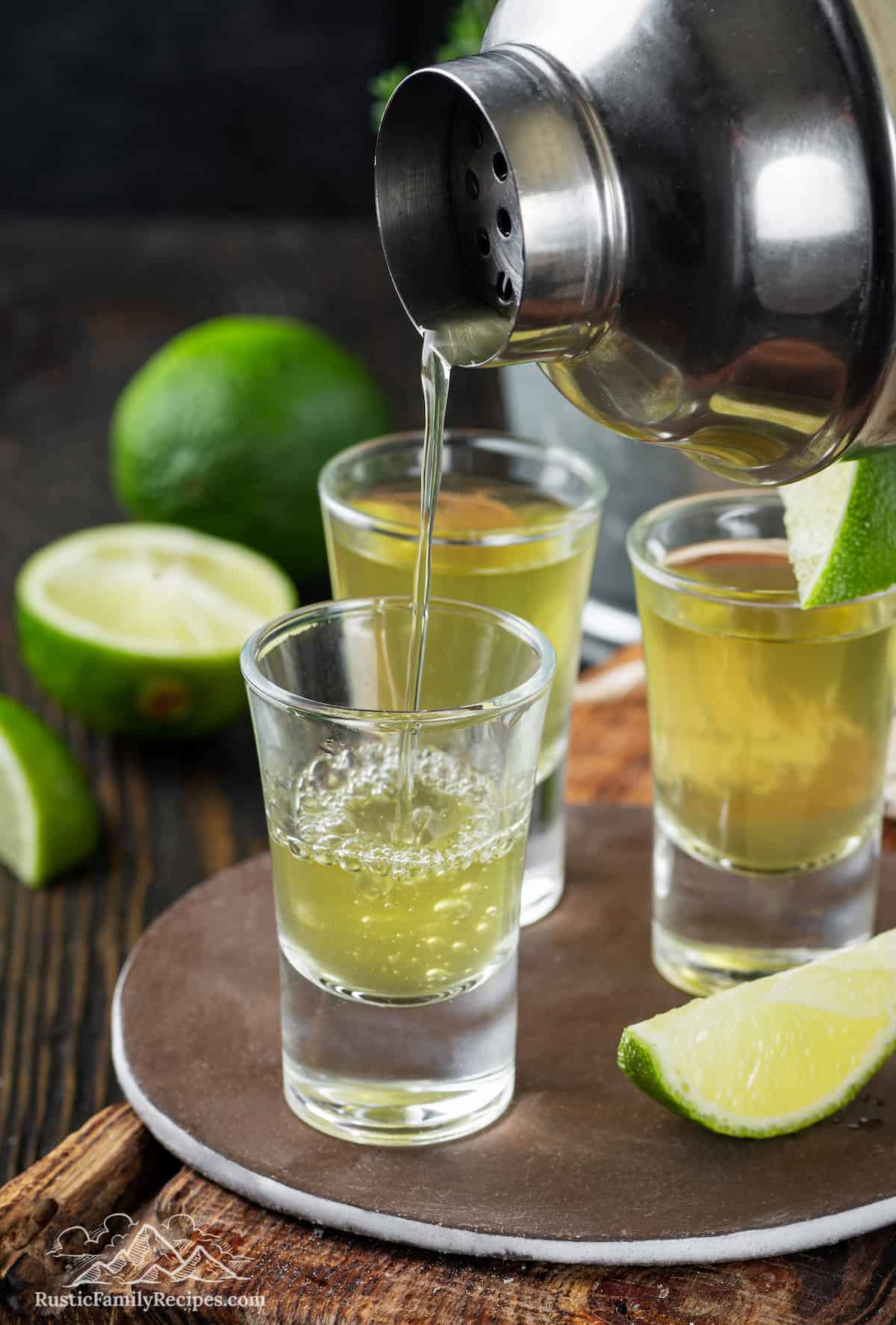 Cocktail shaker pouring green tea shot into glasses