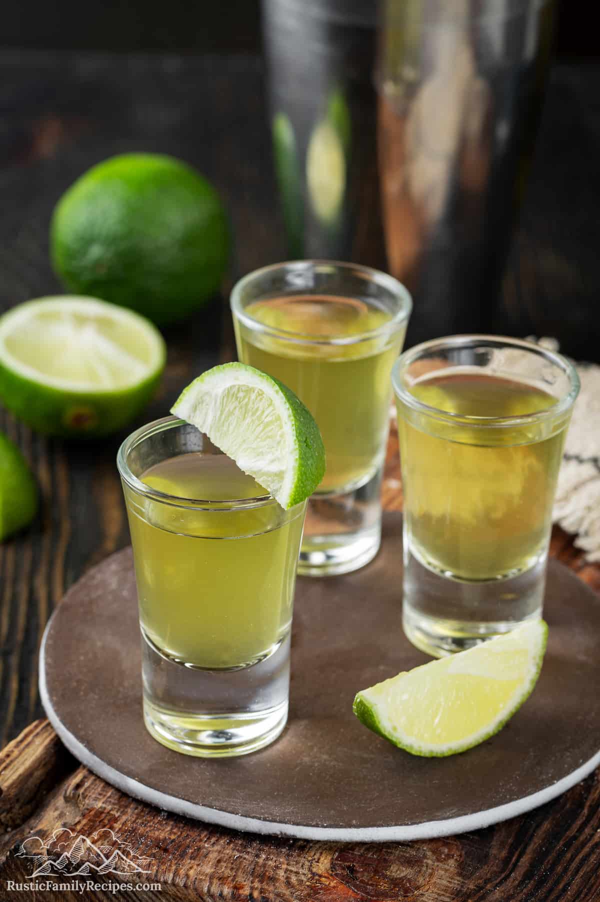 Three shot glasses filled with a green tea shot, with lime wedges