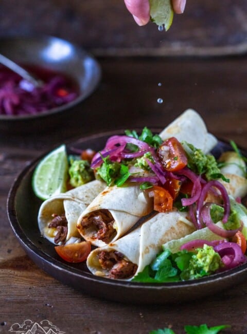 Plate of birria beef flautas with fixings and lime juice being squeezed onto them