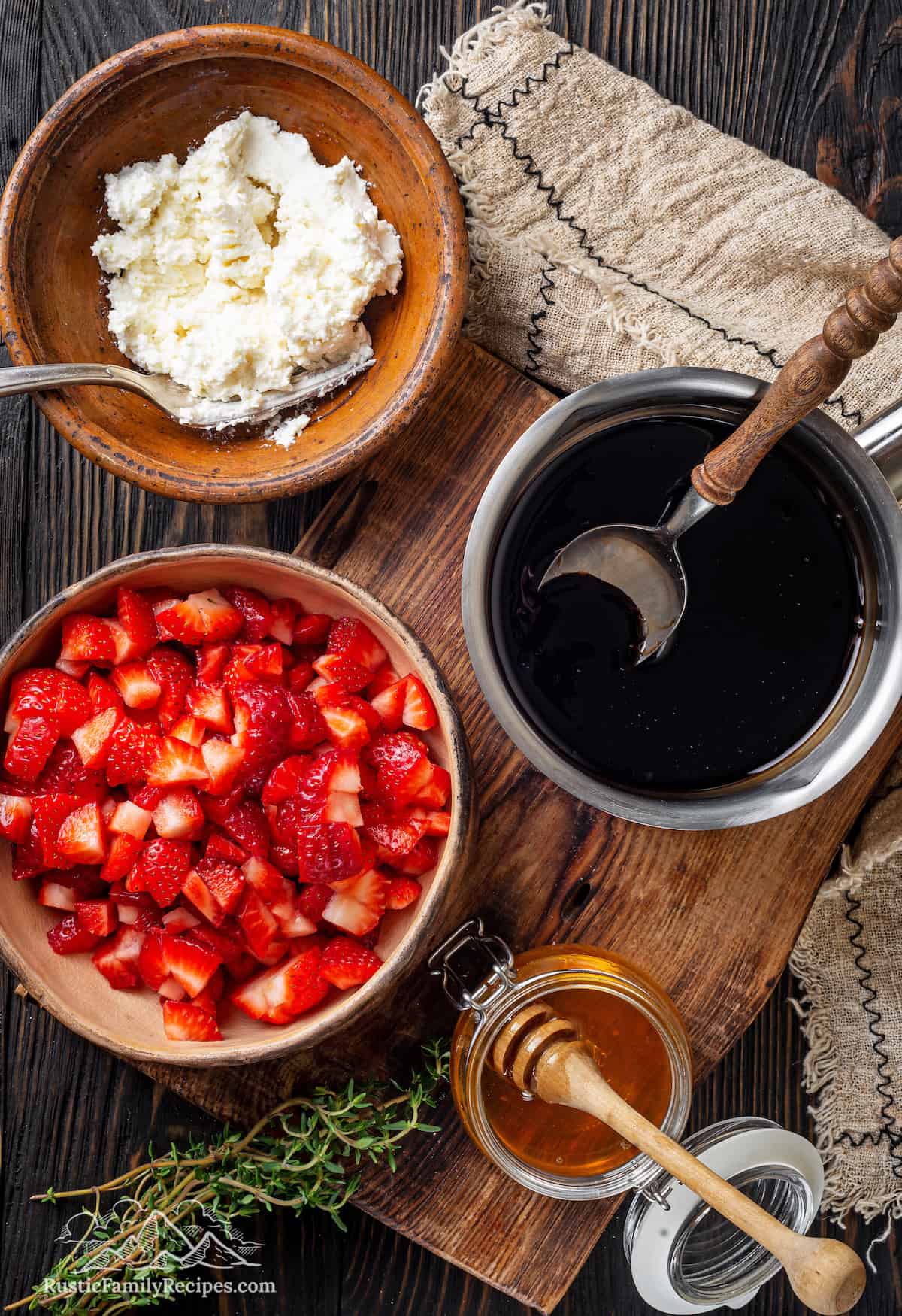 Mixed strawberries in a bowl next to a bowl of goat cheese mix and balsamic glaze