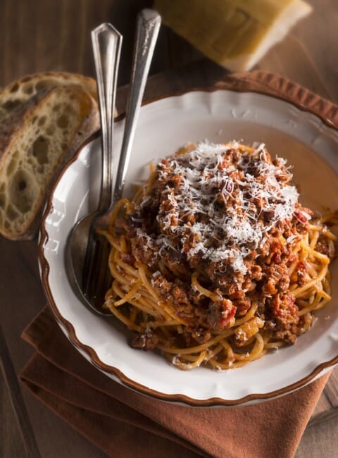 A white bowl filled with bucatini and meat sauce with utensils