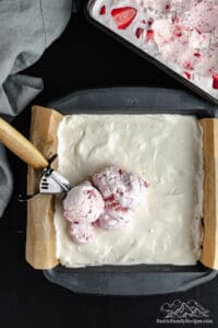 Scoops of strawberry ice cream placed into a baking pan over the crust and vanilla ice cream layers.
