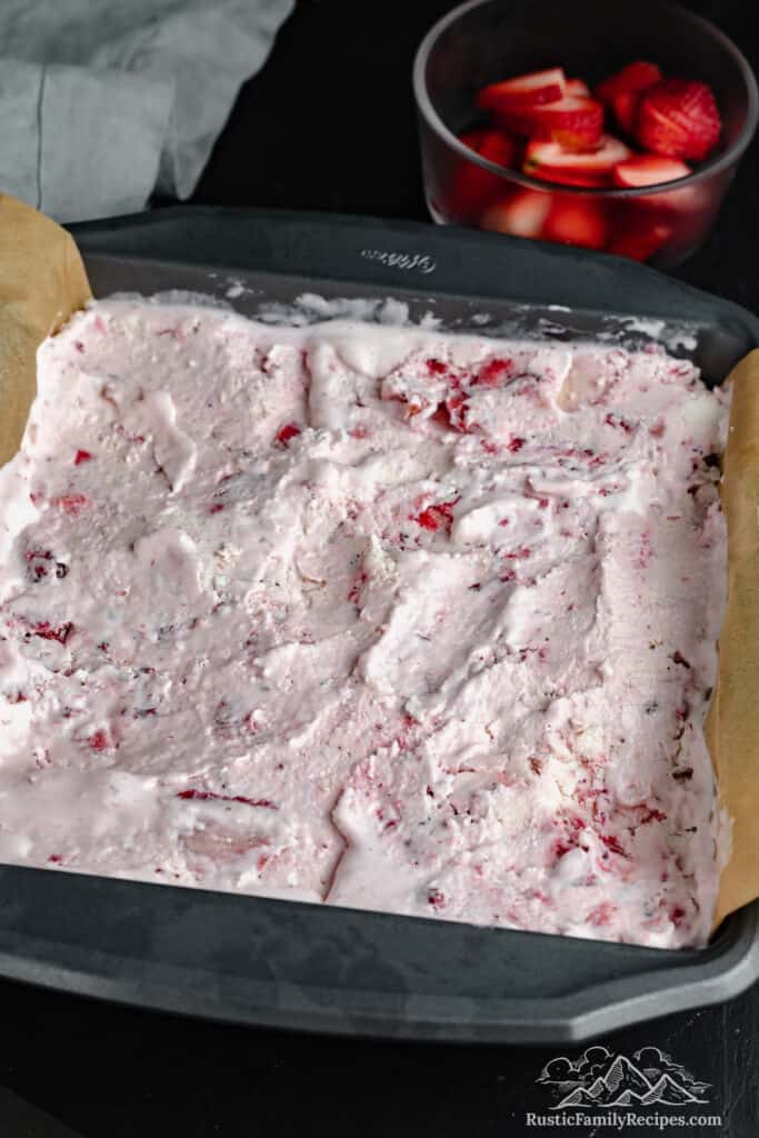 A baking pan filled with the crust, vanilla, and strawberry ice cream layers.