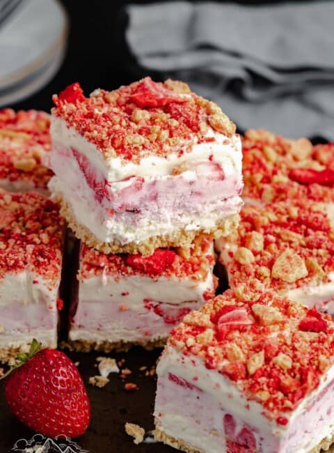 Strawberry shortcake ice cream bars stacked on a wooden cutting board.