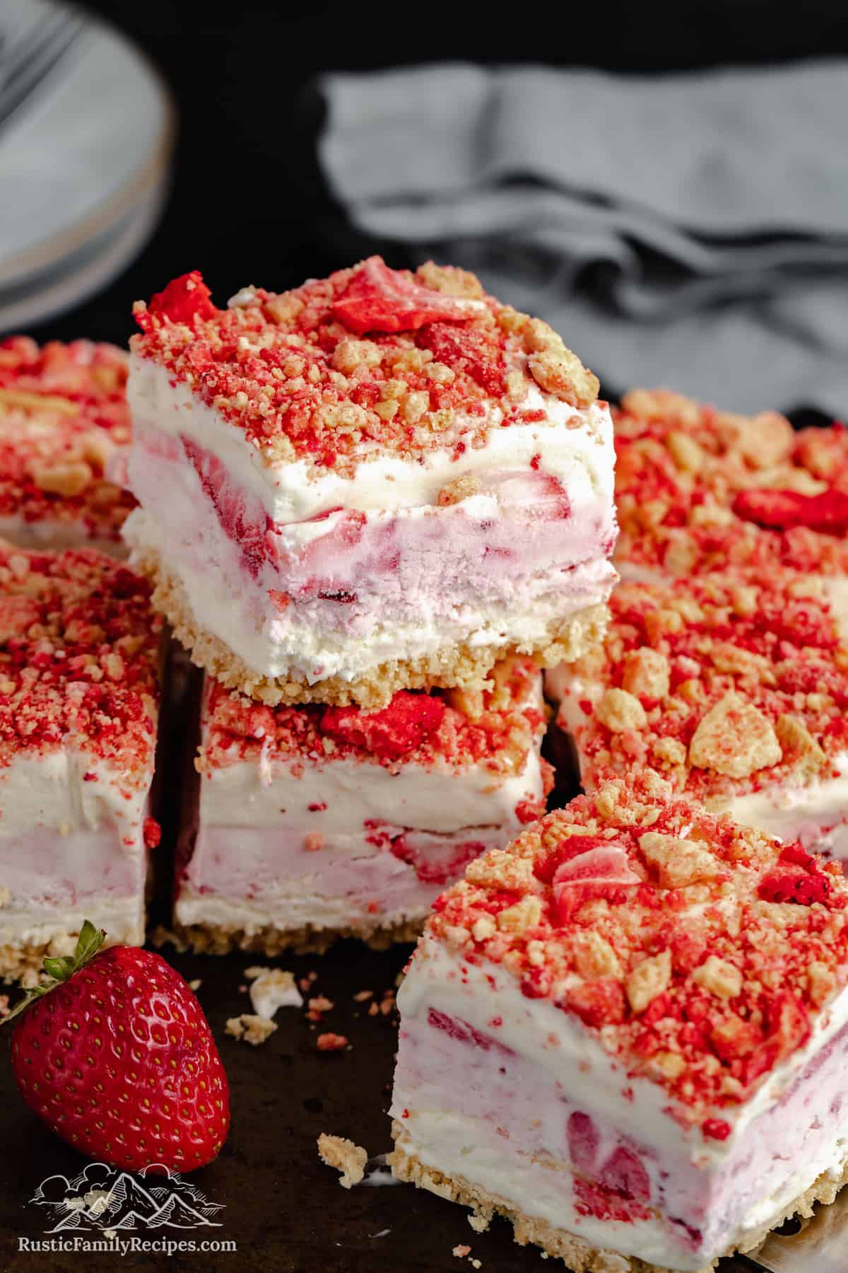 Strawberry shortcake ice cream bars stacked on a wooden cutting board.