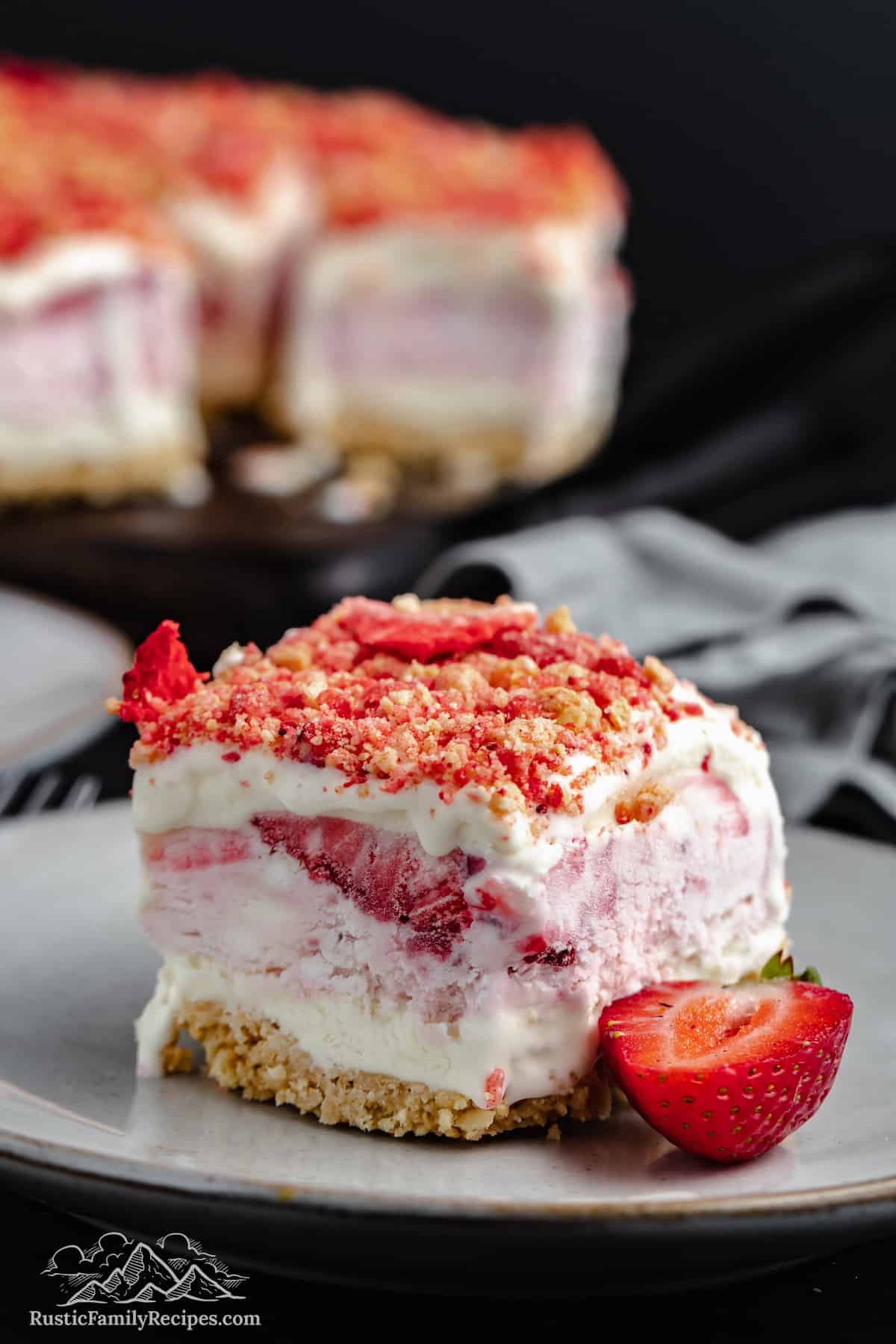 A strawberry shortcake ice cream bar on a plate next to half of a fresh strawberry.