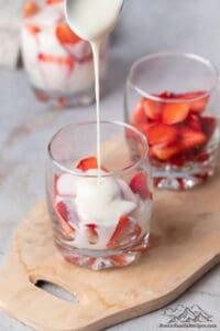 Pouring cream on strawberries in a glass