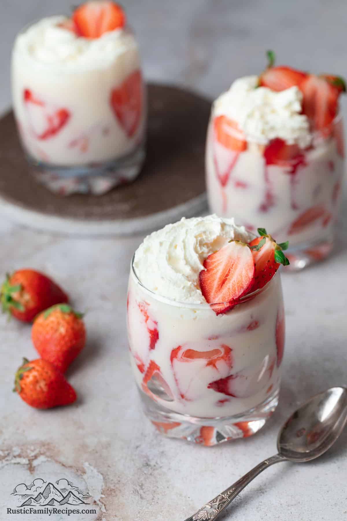 Sliced strawberries, cream and whipped cream in 3 glasses