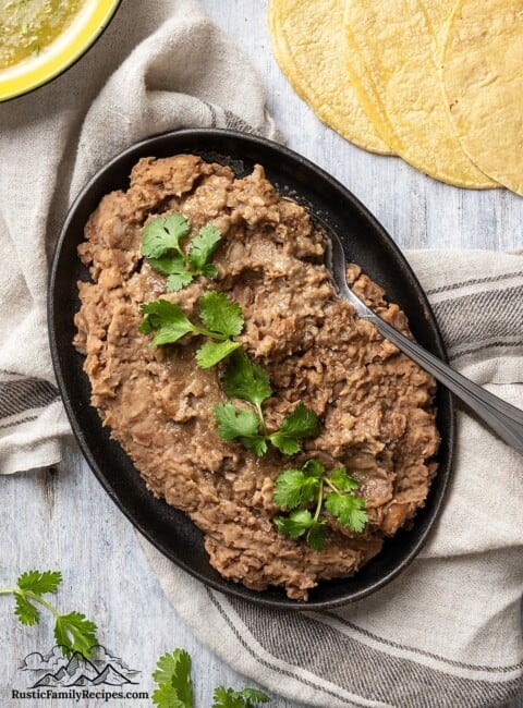 Refried beans in a serving dish next to tortillas